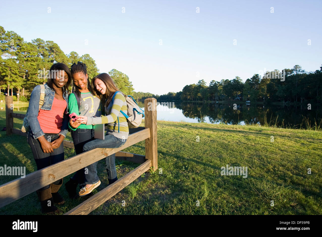 Pre-teen girls sitting on fence, à la tablette à l'ordinateur et téléphone cellulaire, à l'extérieur Banque D'Images