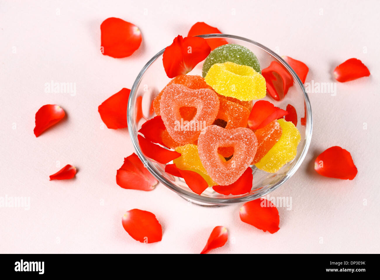 Bonbons colorés avec deux coeurs rouges dans un bol en verre et pétales de rose, vue du dessus Banque D'Images