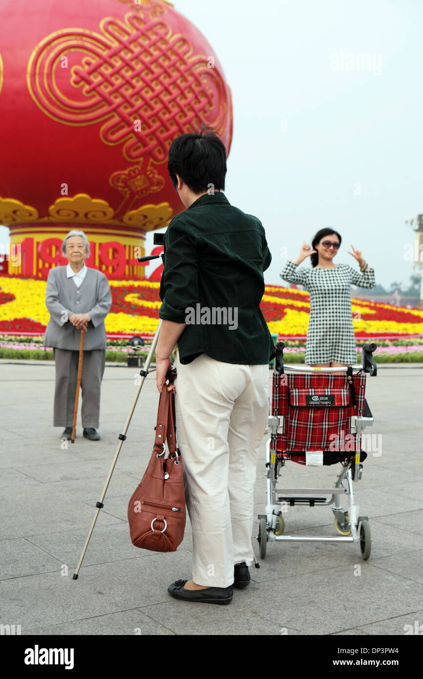 Vieux et jeunes Chinois prendre un autoportrait en face d'un communisme affichage commémorative, la Place Tiananmen, à Beijing, Chine. Banque D'Images