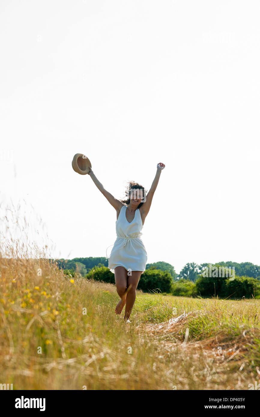 Little girl holding straw hat avec les bras en l'air, marcher dans la zone un jour d'été, Allemagne Banque D'Images