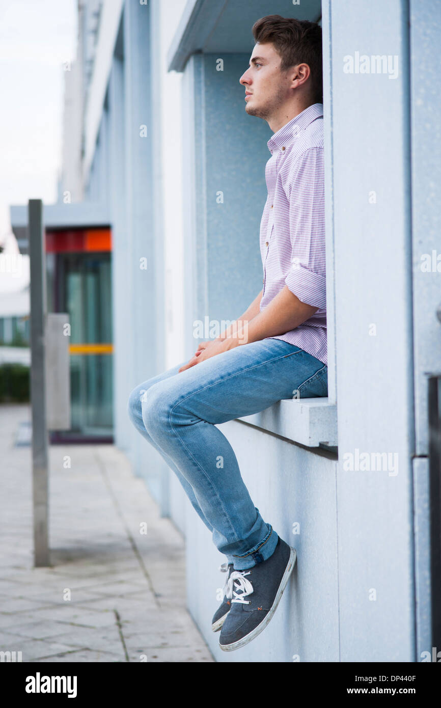 Jeune homme assis sur le rebord extérieur, Allemagne Banque D'Images