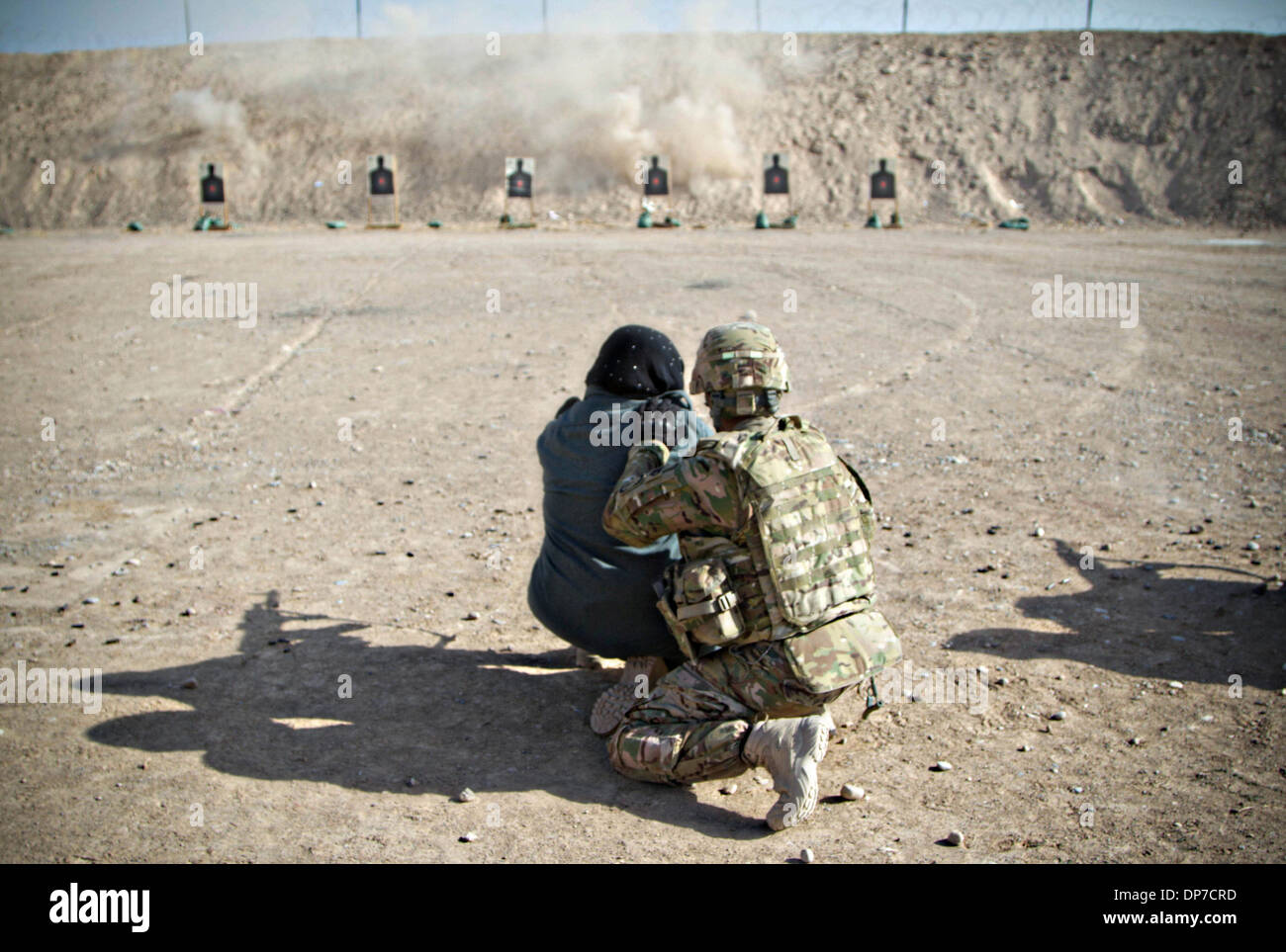 Une femme soldat de l'armée américaine forme une Police nationale afghane recruter portant des couvre-chef en tirant une AK-47 lors des qualifications à la Police nationale afghane régional conjoint Center 7 décembre 2013 à Kandahar, en Afghanistan. Banque D'Images