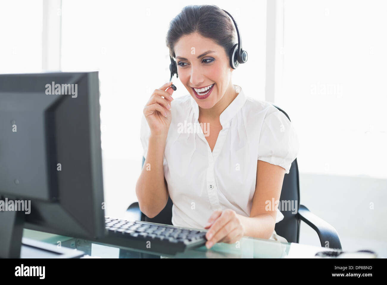 Laughing call centre agent assise à son bureau sur un appel Banque D'Images