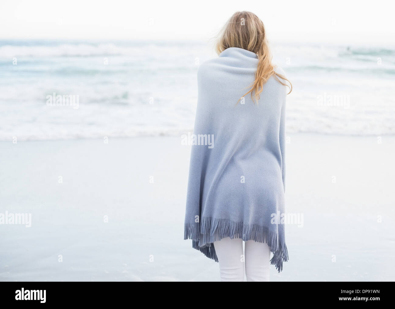 Vue arrière d'une femme blonde se réchauffer dans une couverture Banque D'Images