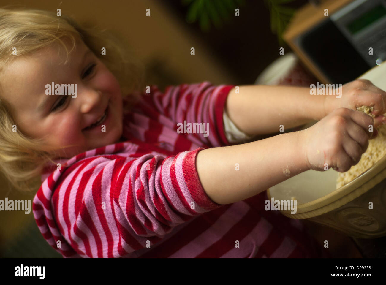 Smiling little girl effrite pâtisserie dans un bol à mélanger. Banque D'Images
