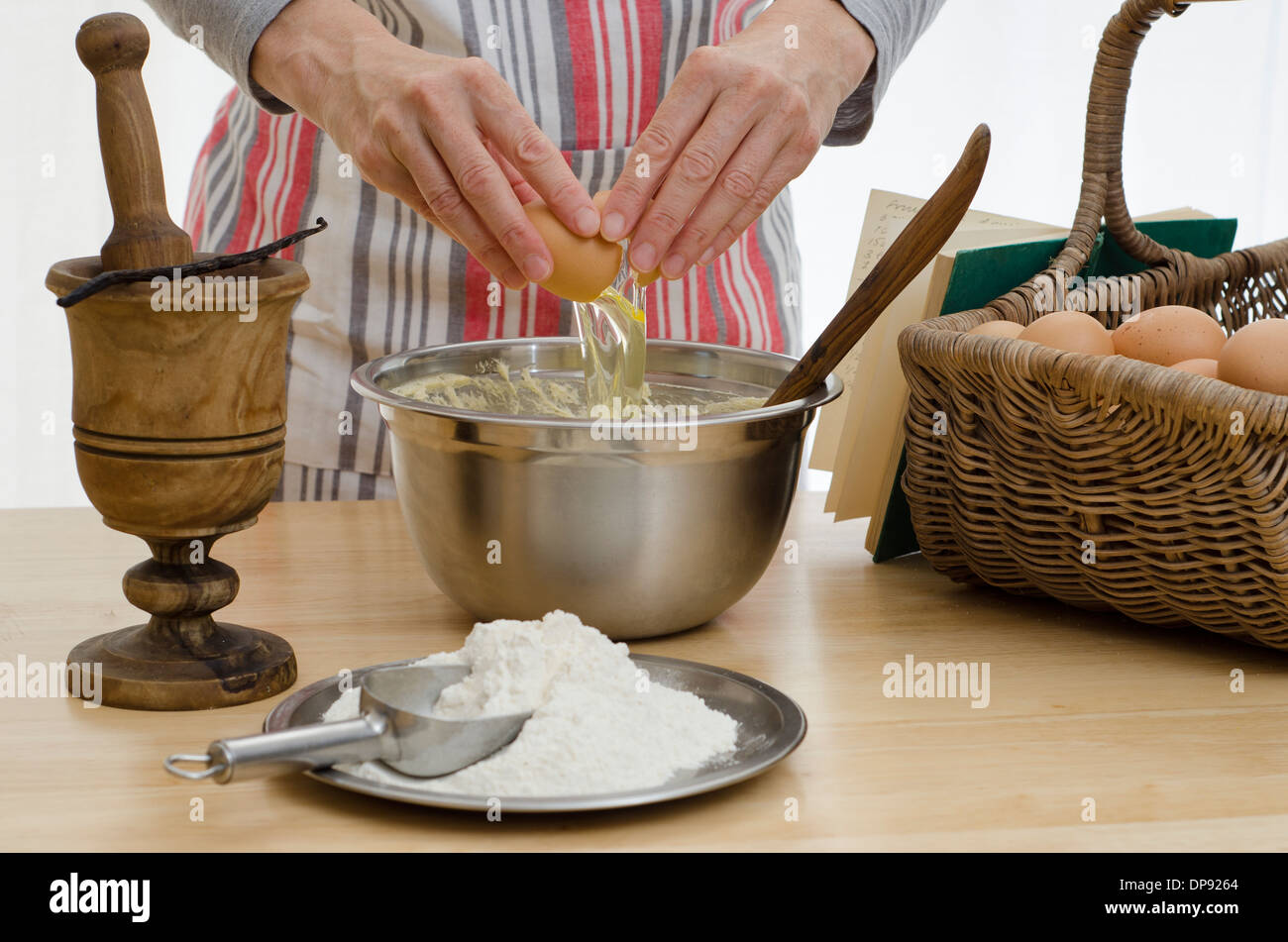 L'ajout de mains dans un bol d'œufs, entouré par les autres composants et un livre de recettes. Banque D'Images