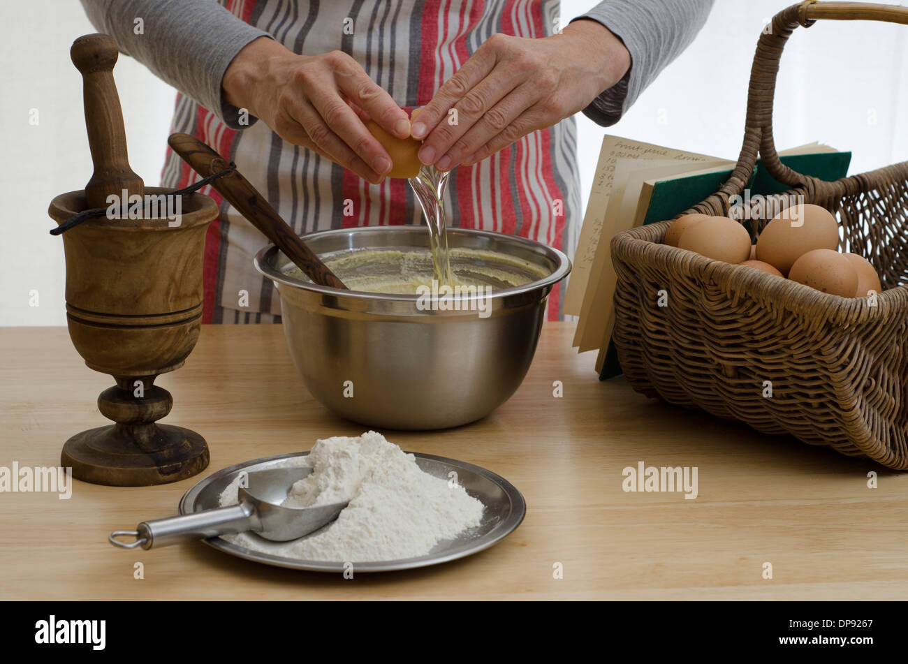 La femme d'un gâteau, l'ajout d'un oeuf dans un bol, entouré par les autres ingrédients. Banque D'Images