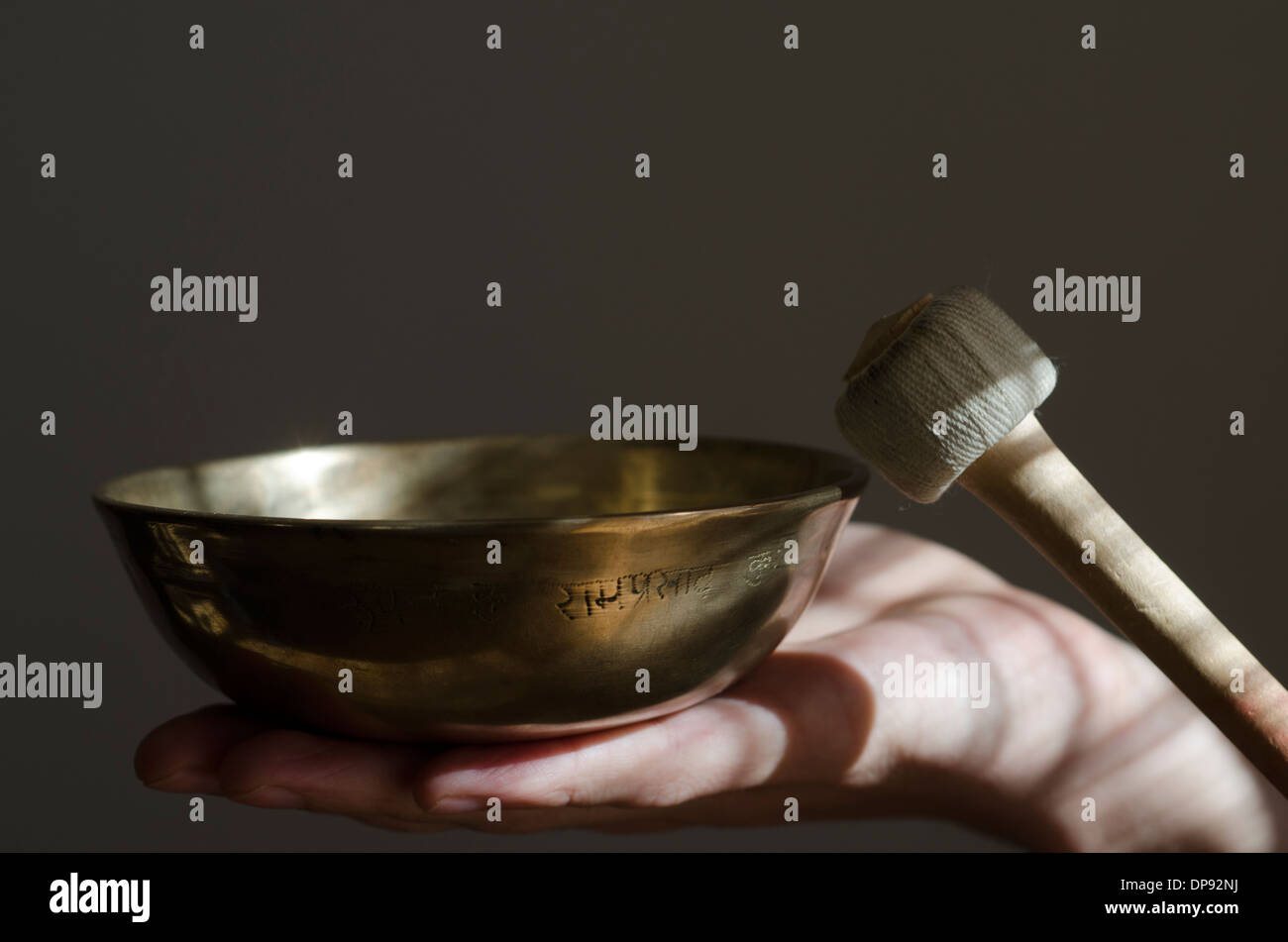 Un bol chantant tibétain assis dans une main se joue avec un bâton. Banque D'Images