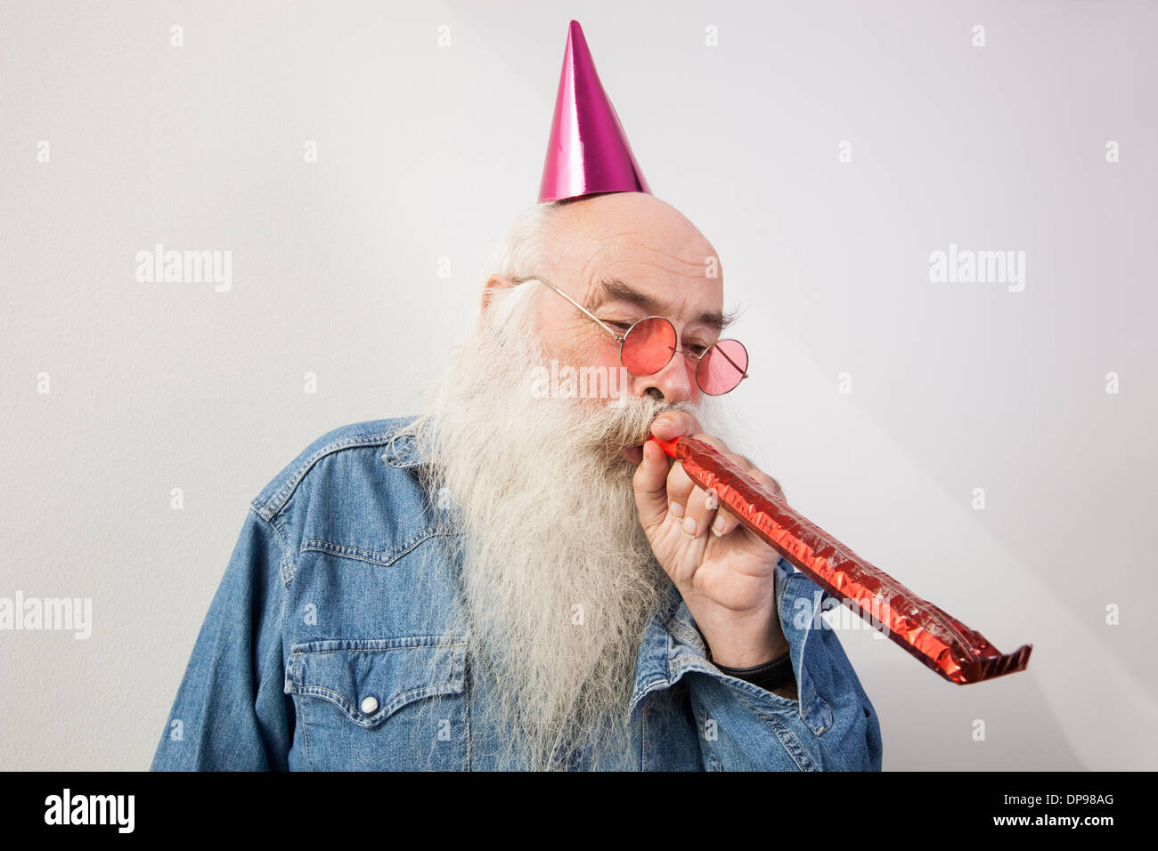 Senior man wearing party hat tout en soufflant corne contre fond gris Banque D'Images