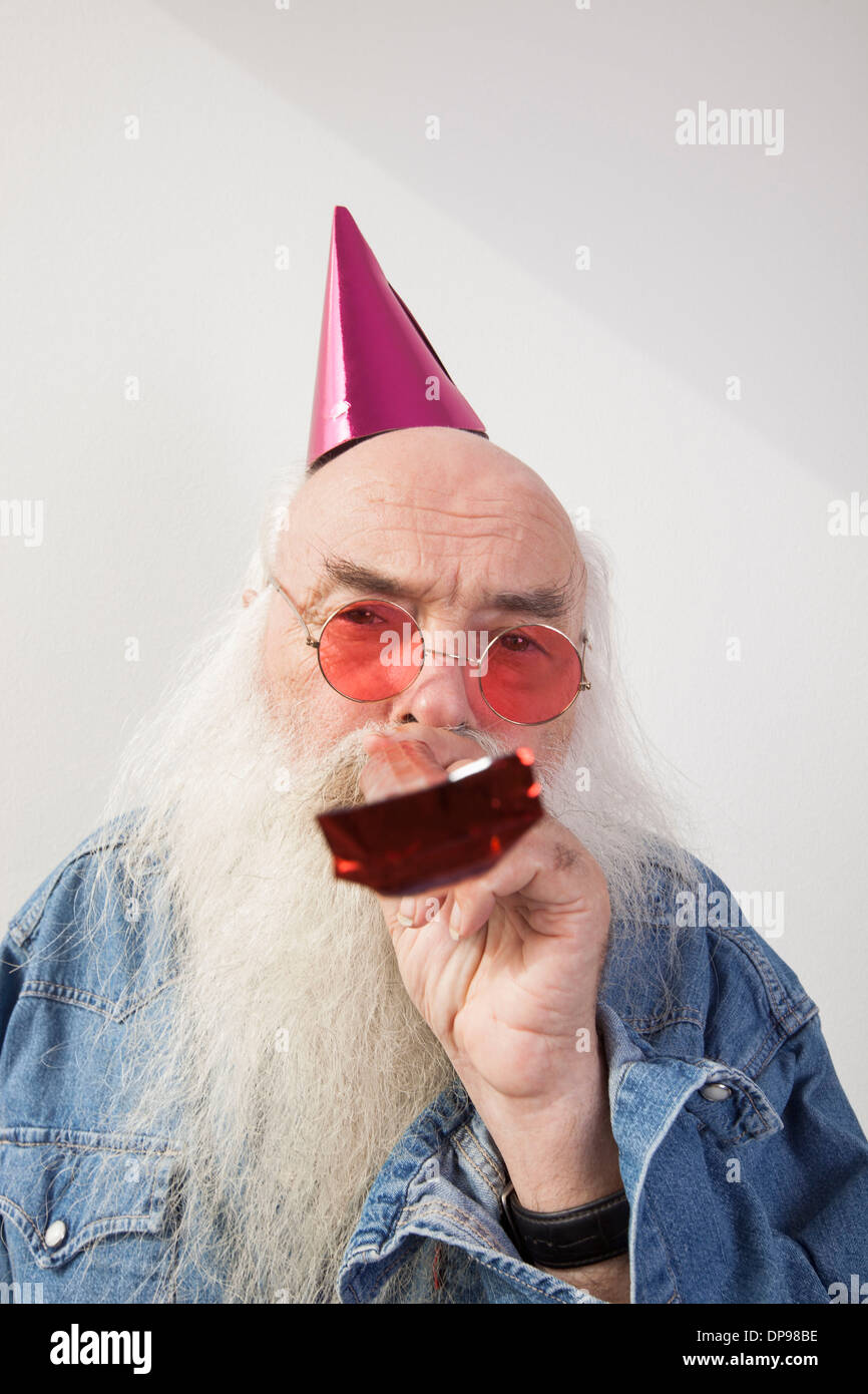 Portrait of senior man wearing party hat et red verres tout en soufflant corne contre fond gris Banque D'Images