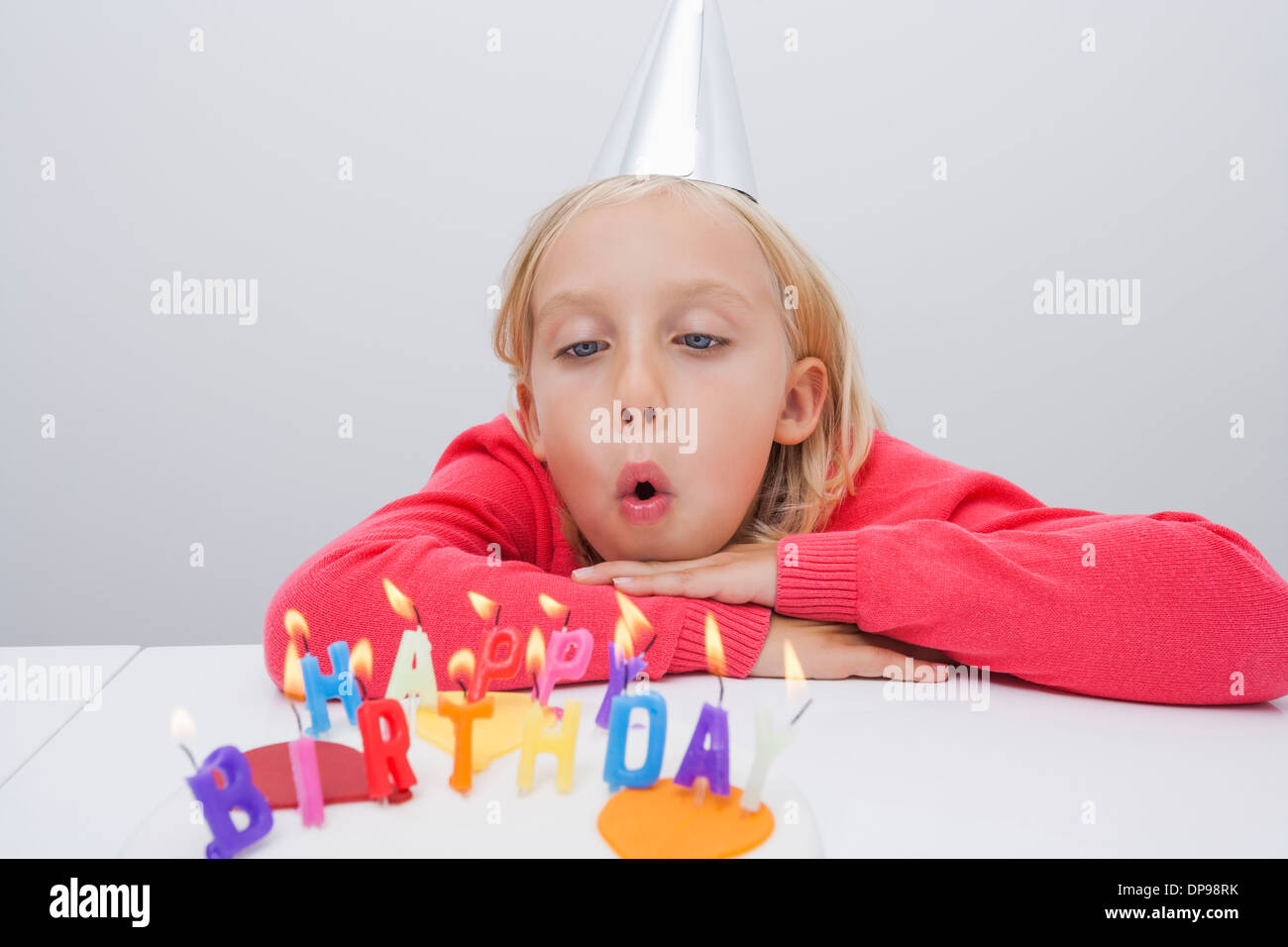 Girl blowing birthday candles at table in house Banque D'Images
