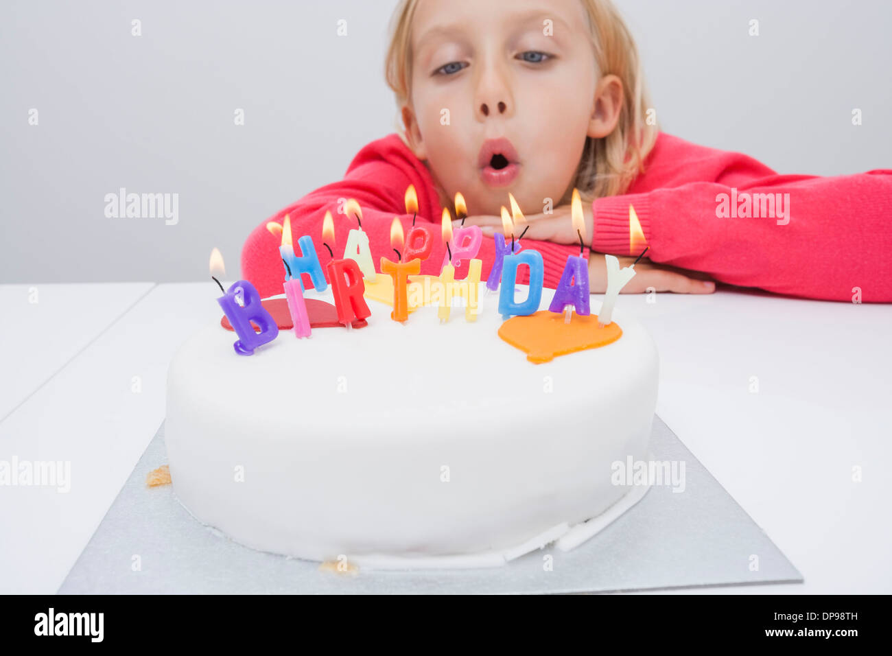 Cute girl blowing birthday candles at table in house Banque D'Images
