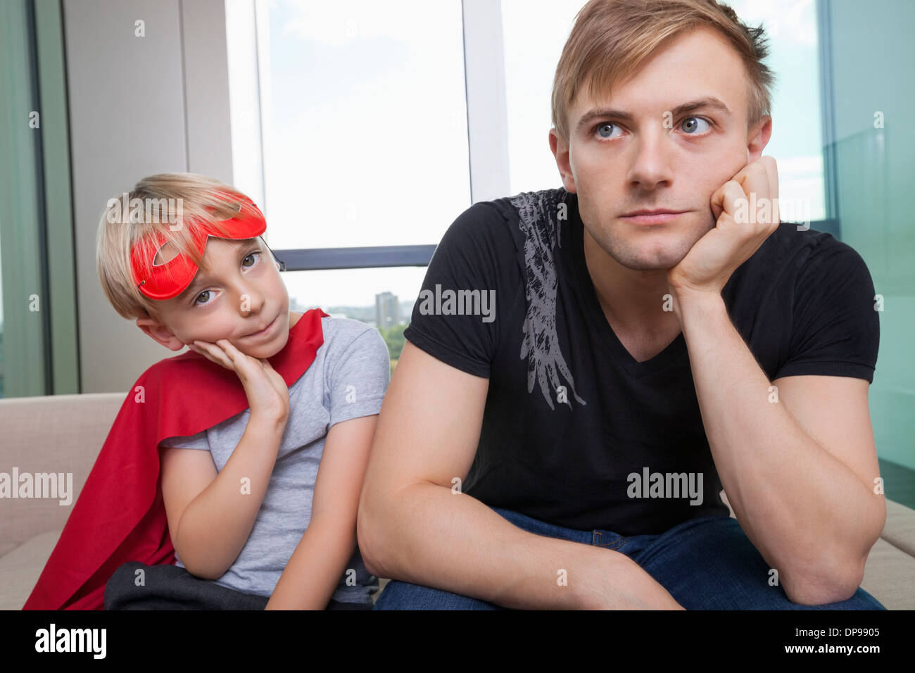 Portrait de triste garçon habillé en costume de super-héro assis avec le père sur le canapé-lit à la maison Banque D'Images