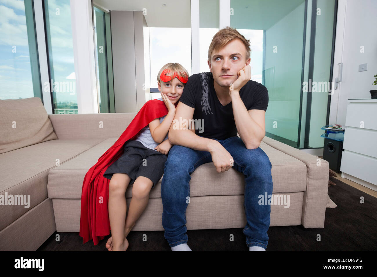 Portrait of smiling boy habillés en costume de super-héro assis avec triste père sur un canapé-lit à la maison Banque D'Images
