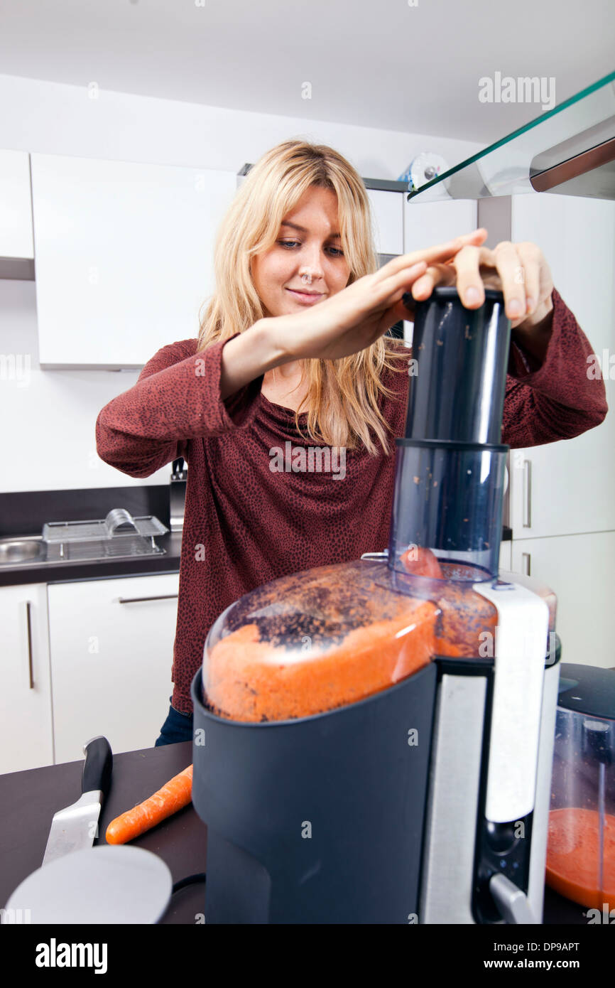 Jeune femme un jus de carottes dans la cuisine Banque D'Images