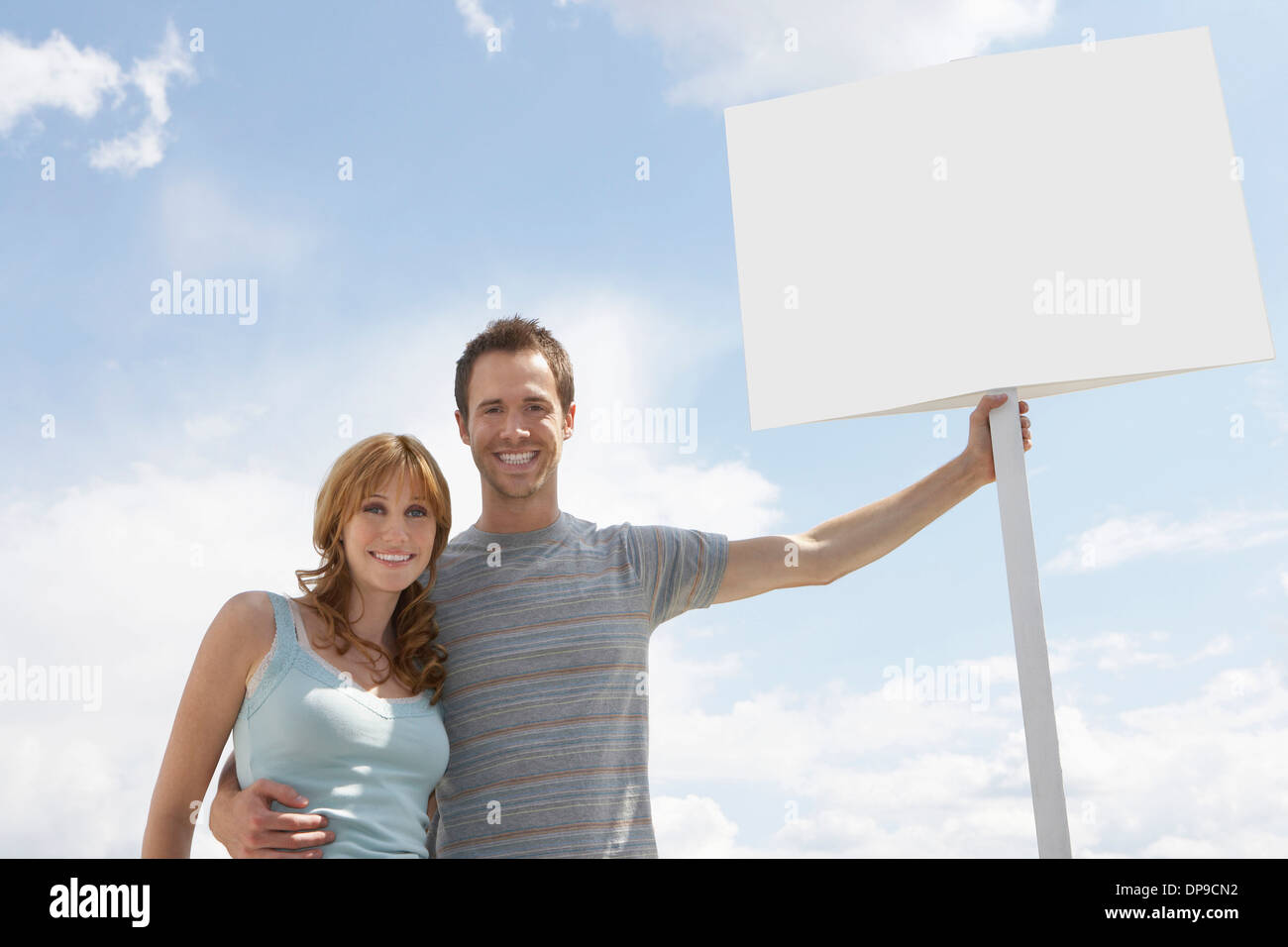 Portrait of happy couple with blank sign board contre ciel nuageux Banque D'Images
