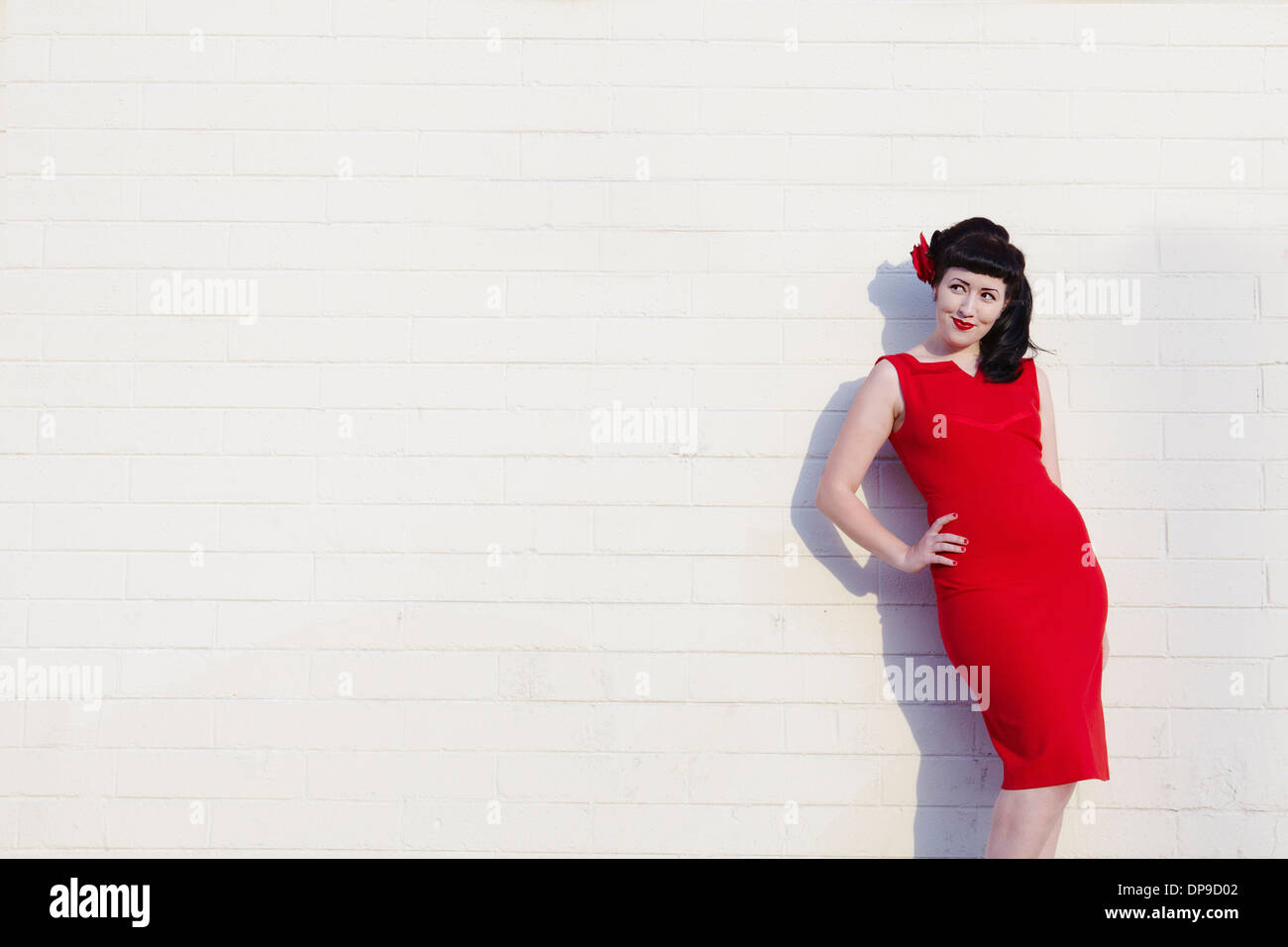 Belle jeune femme en robe rouge leaning on wall Banque D'Images