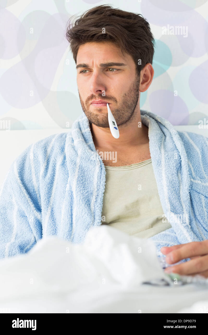 Homme malade avec le thermomètre dans la bouche sitting on bed Banque D'Images
