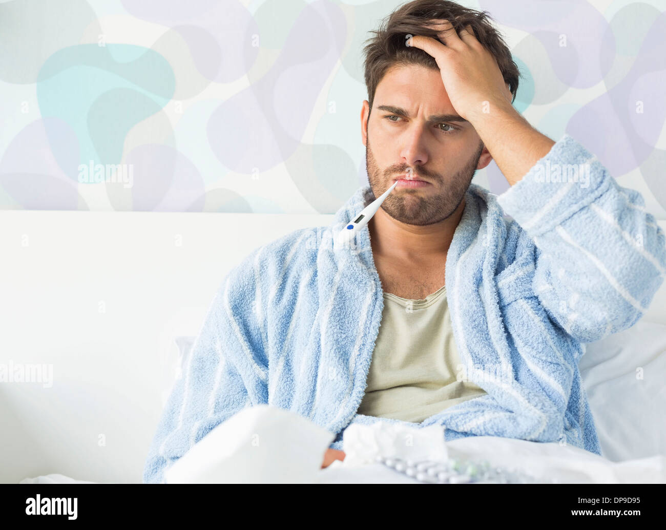 Homme malade avec le thermomètre dans la bouche assis sur le lit à la maison Banque D'Images