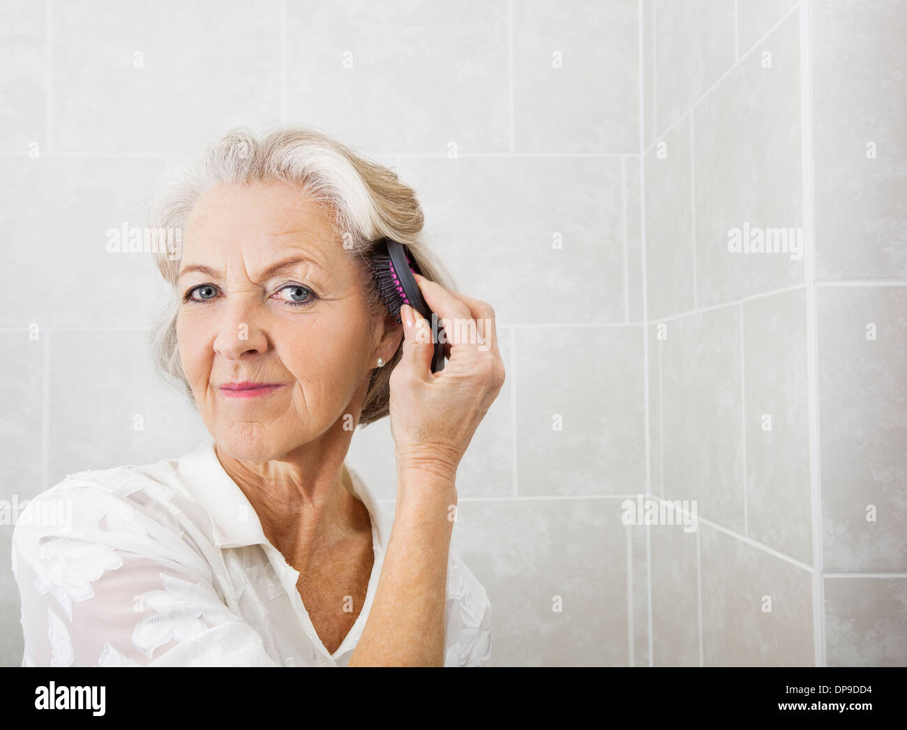 Portrait of senior woman brushing cheveux dans salle de bains Banque D'Images