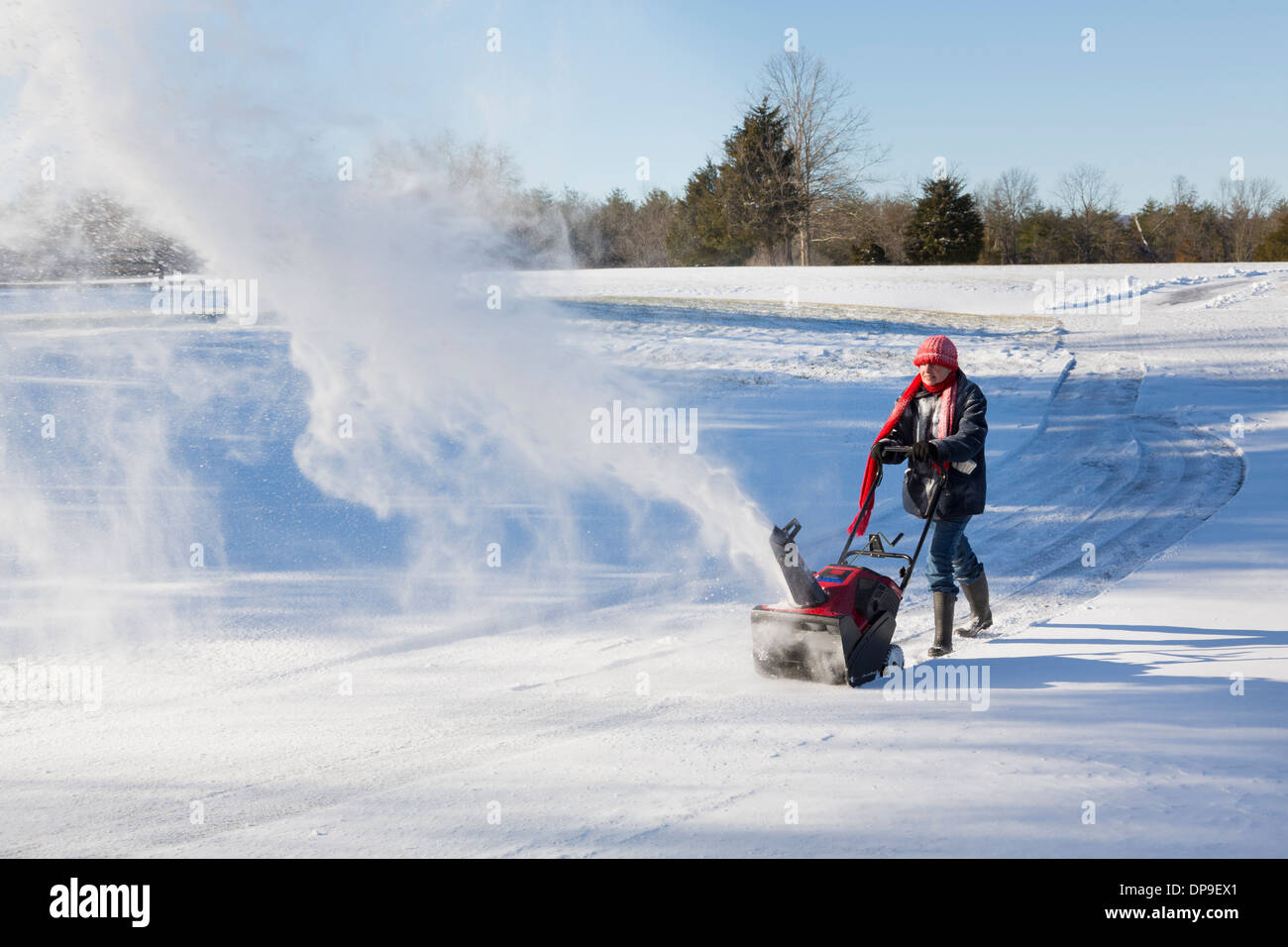 Femme à l'aide d'une souffleuse à neige sur la route rurale par un jour de vent Banque D'Images
