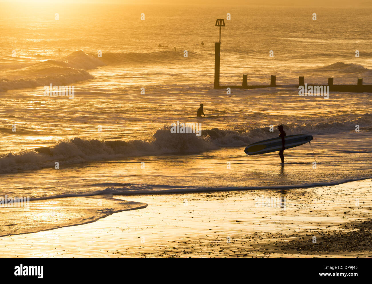 Debout sur le rivage Surfer holding his surfboard regardant la mer au coucher du soleil sur la plage de Boscombe dans le Dorset, Angleterre, RU Banque D'Images