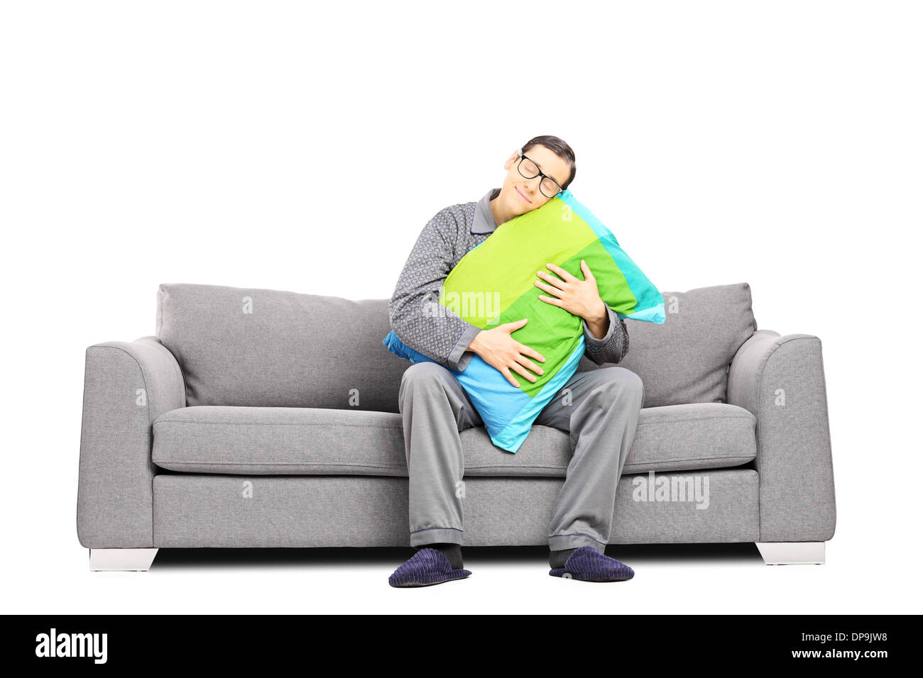 Sleepy guy en pyjama, assis sur le canapé embrassant un oreiller Banque D'Images