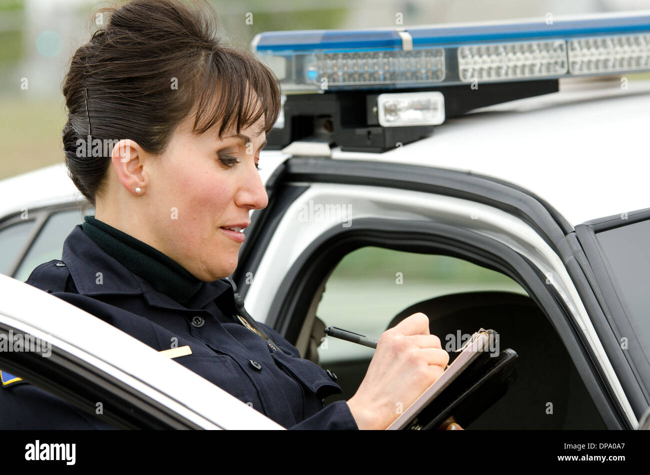 Une femme agent de police écrit un billet tout en vous tenant à côté de sa voiture de patrouille. Banque D'Images