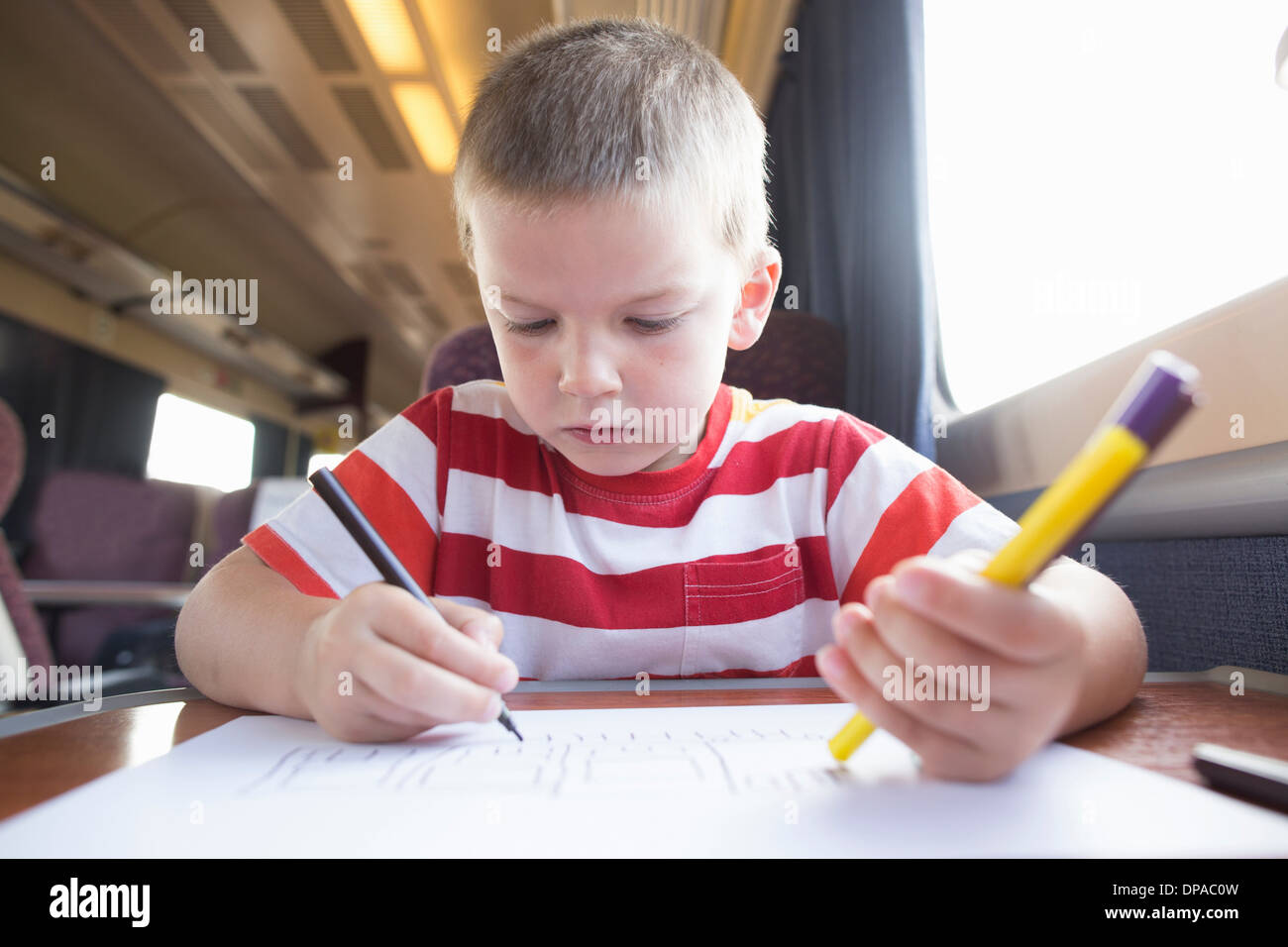 Jeune garçon avec un crayon, un stylo et du papier sur le train Banque D'Images