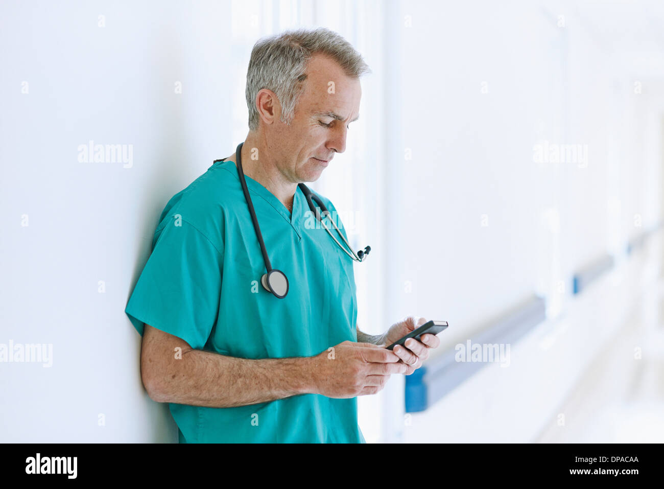 Surgeon standing in corridor looking at smartphone Banque D'Images