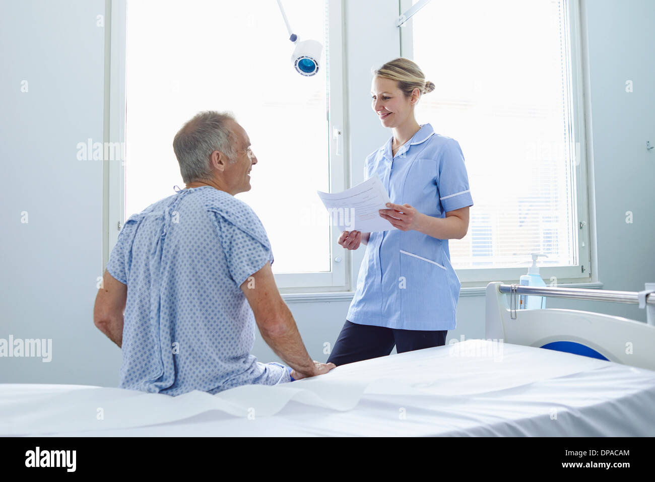 Nurse talking to patient sitting on hospital bed Banque D'Images