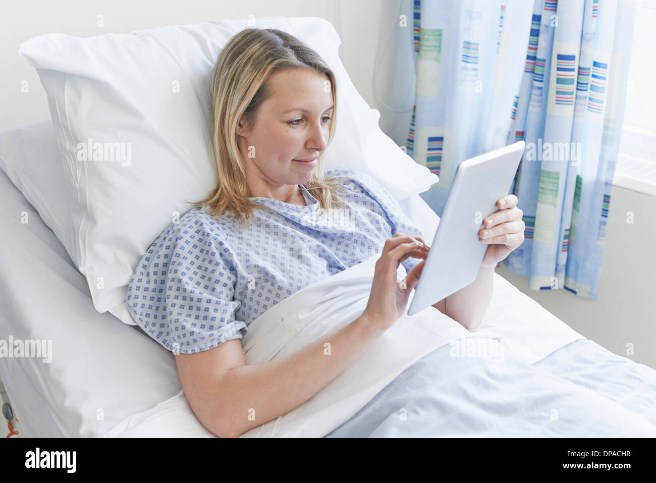 Patient lying on hospital bed using digital tablet Banque D'Images