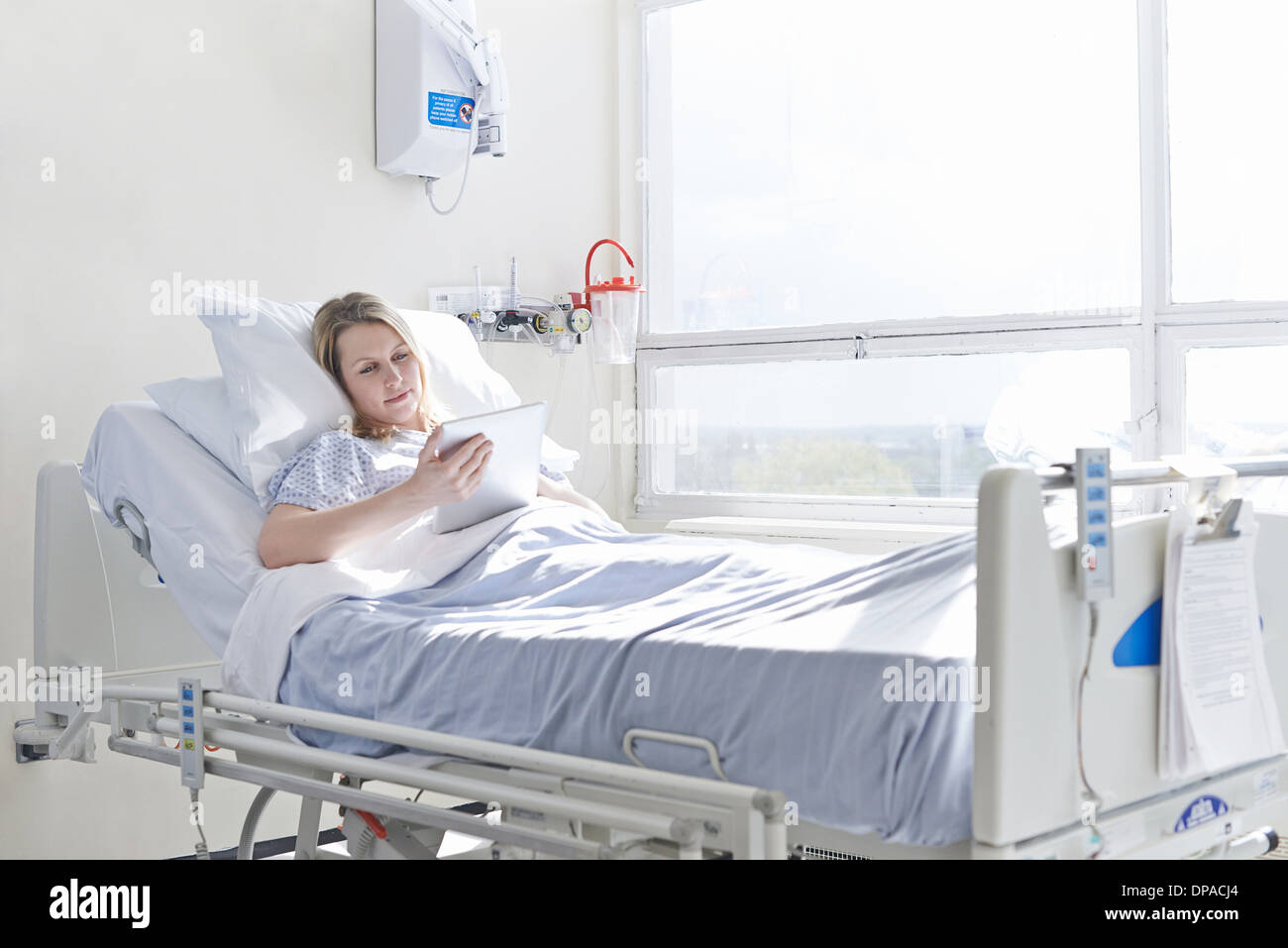 Patient lying on hospital bed using digital tablet Banque D'Images
