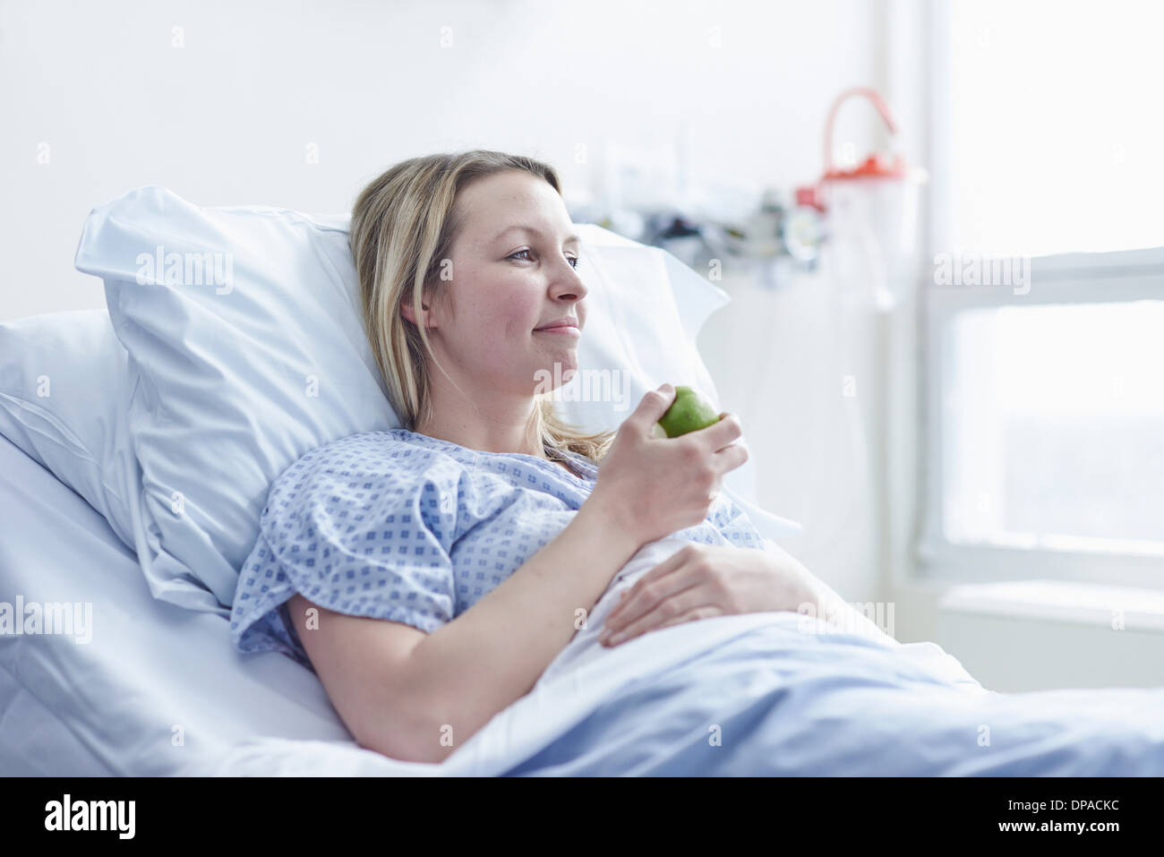 Patient lying in hospital bed eating apple Banque D'Images