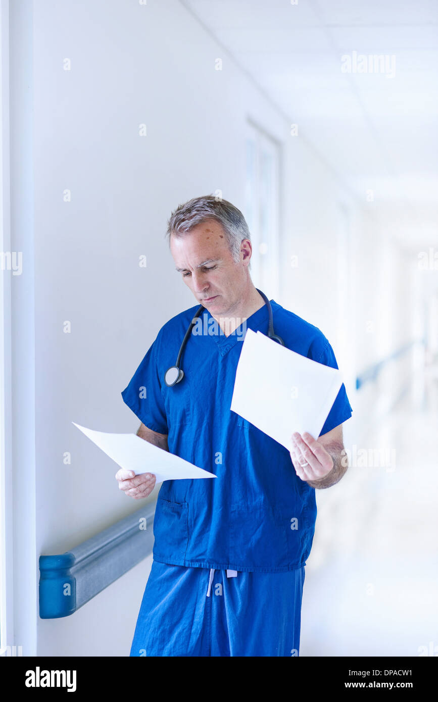 Doctor standing in corridor reading medical records Banque D'Images