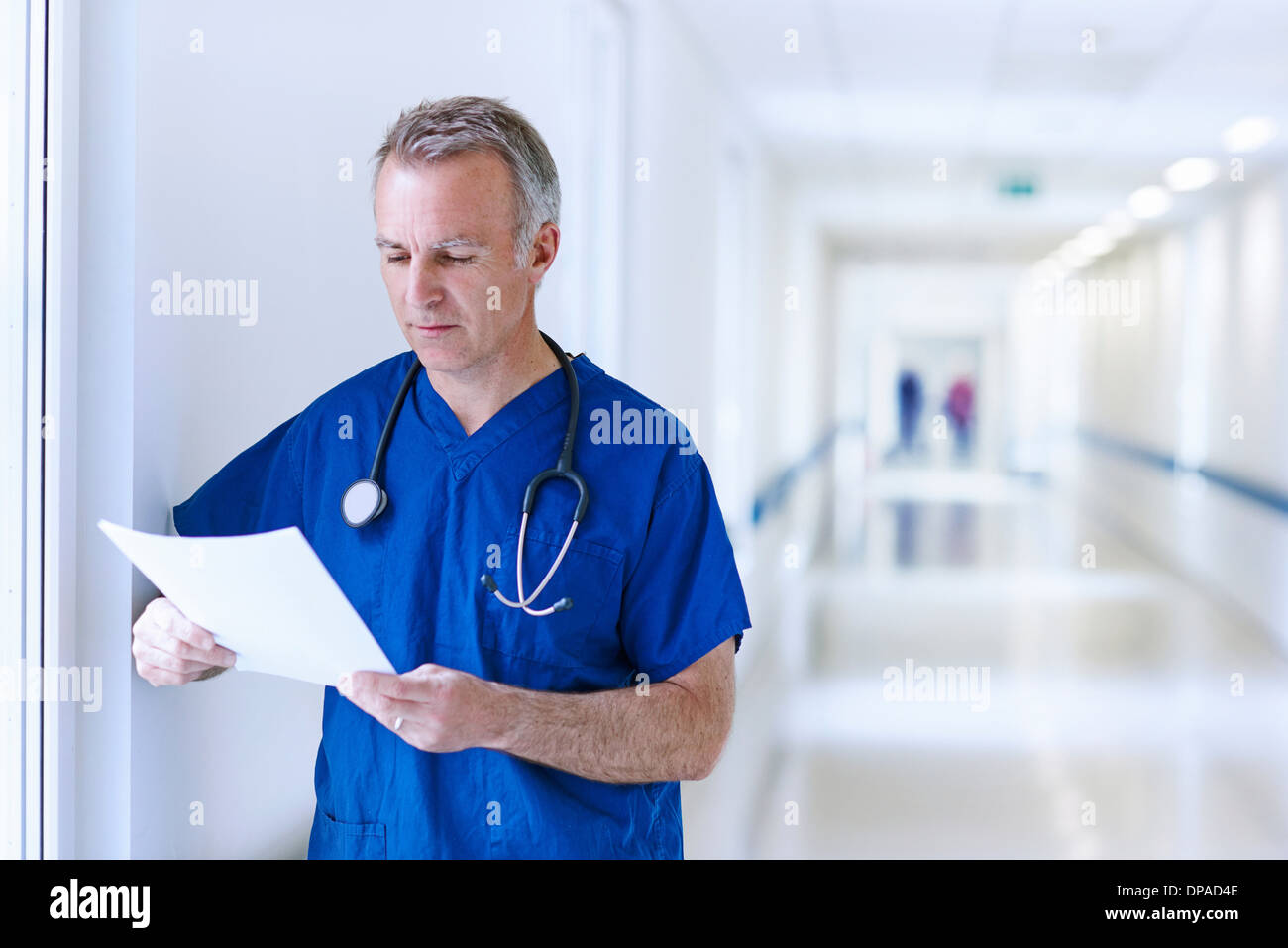 Doctor standing in corridor reading medical records Banque D'Images