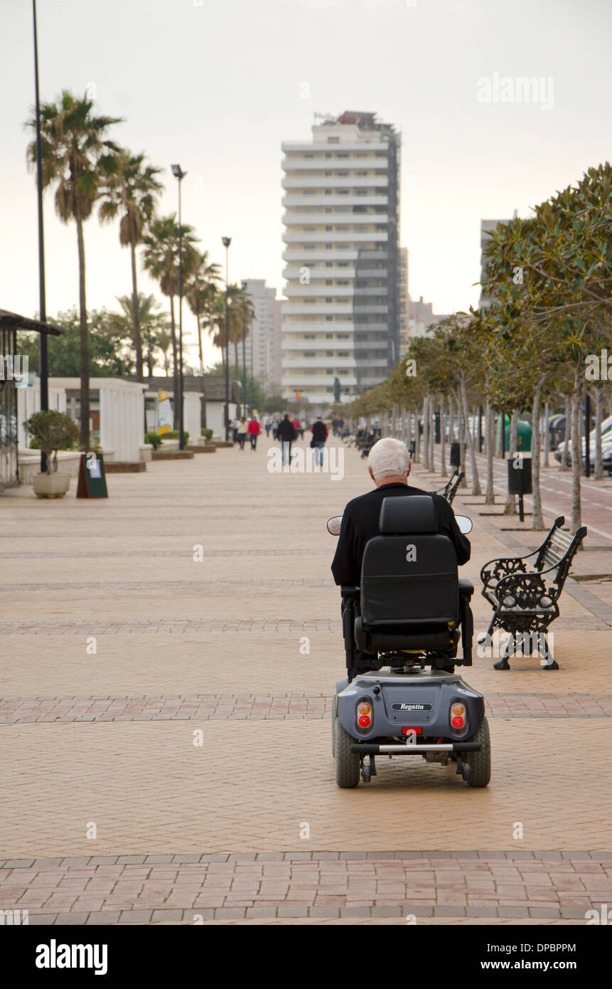 Man en fauteuil roulant motorisé, sur le boulevard de Fuengirola, Costa del Sol, Espagne. Banque D'Images