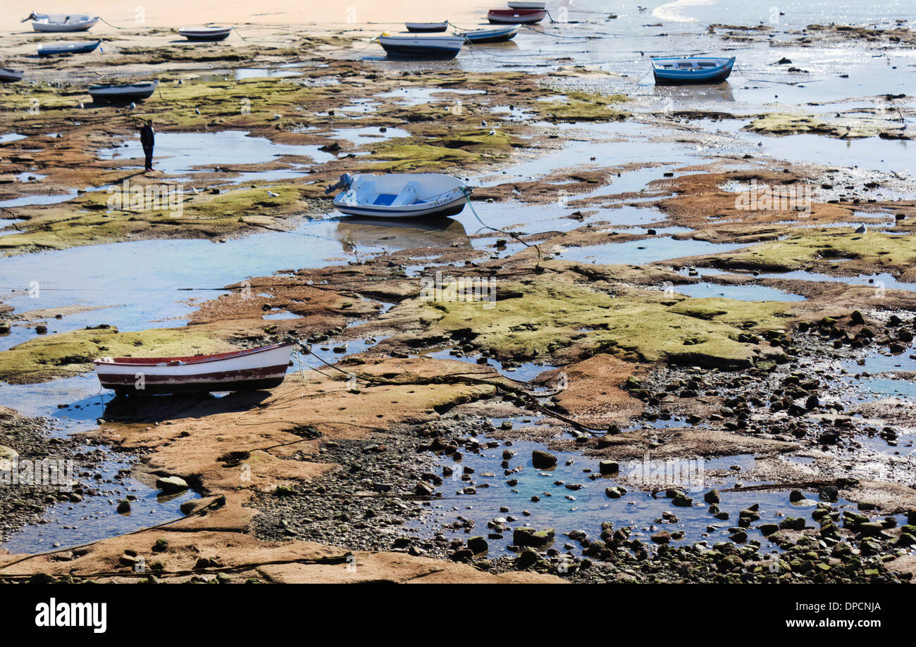 Cadix, Espagne. Figure solitaire parmi les petits bateaux de pêche sur la plage à marée basse. Banque D'Images