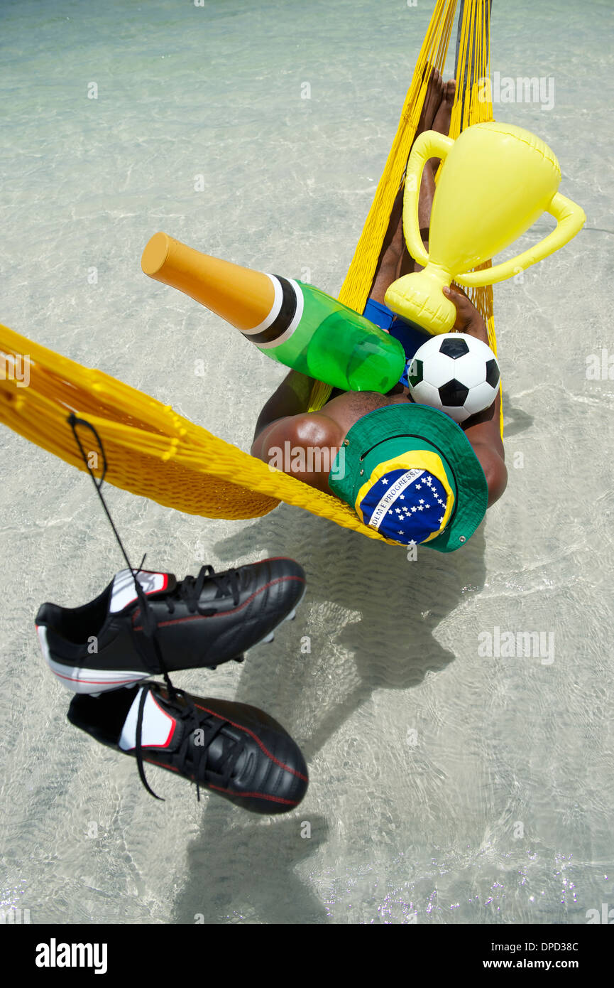 Joueur de football brésilien, Champion de célébrer en vous reposant dans un hamac avec un ballon de football, bouteille de champagne, et le trophée Banque D'Images