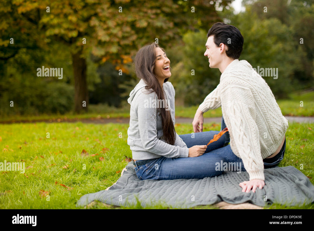 Jeune couple on blanket in park, laughing Banque D'Images
