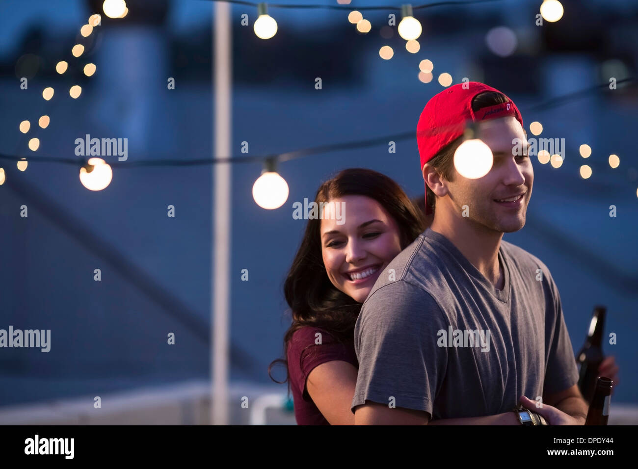 Jeune couple hugging at rooftop barbecue Banque D'Images