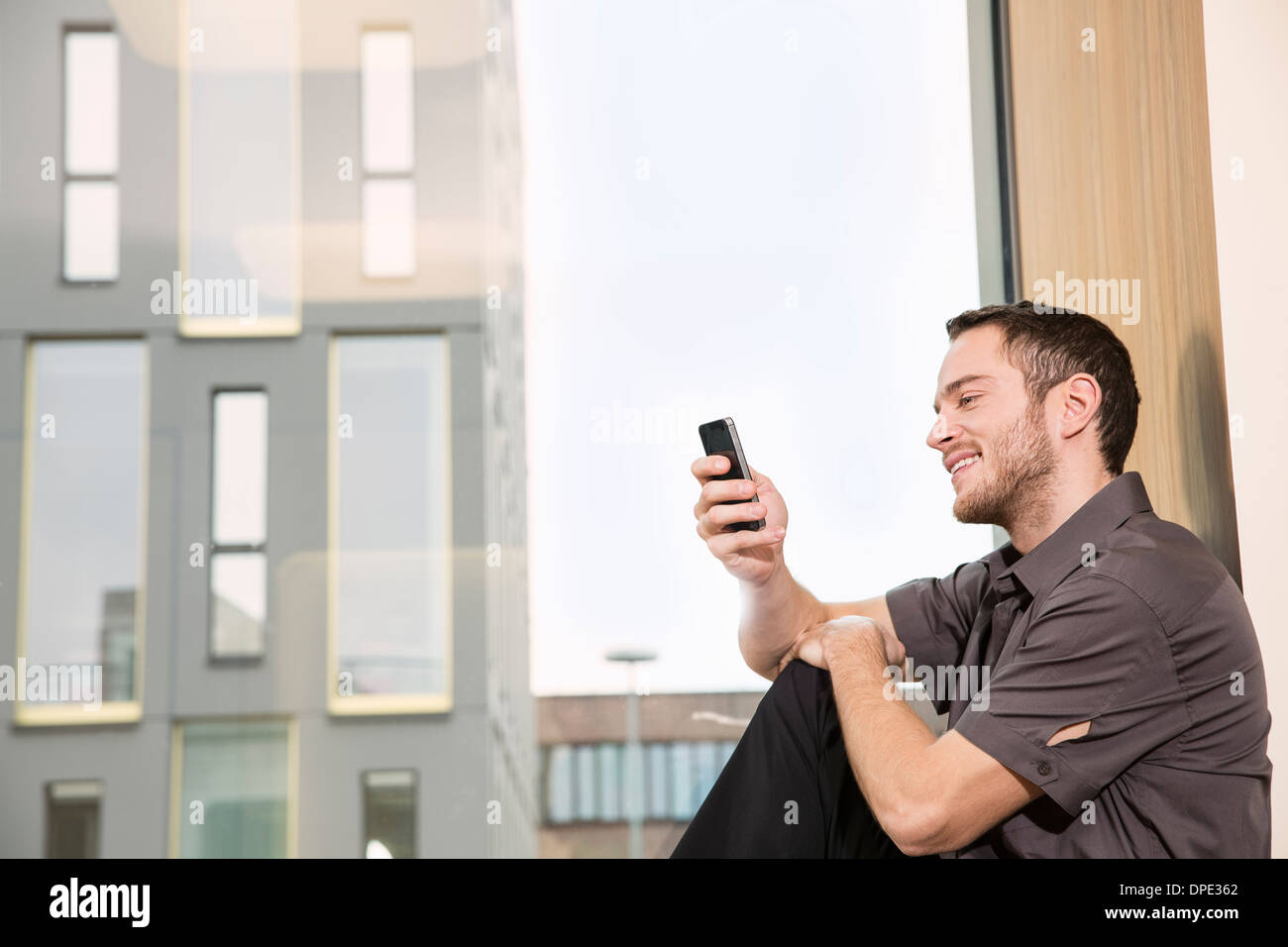 Businessman sitting on windowsill using smartphone Banque D'Images