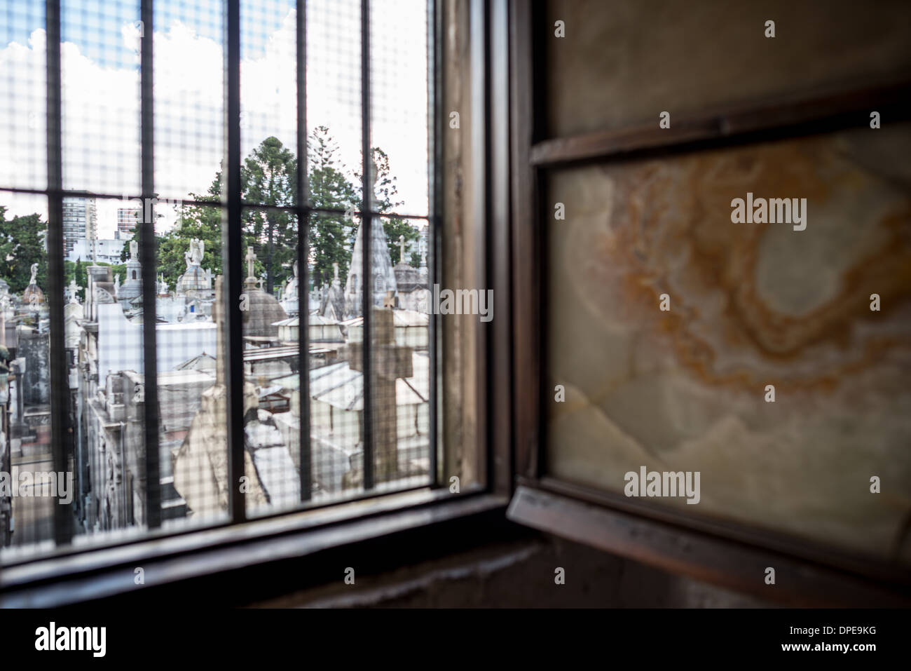 BUENOS AIRES, Argentine — Une vue à travers l'une des fenêtres originales de l'époque coloniale de la Basílica de Nuestra Señora del Pilar révèle le cimetière historique de Recoleta au-delà. Le cimetière, créé en 1822, jouxte l'église de 1732 et compte parmi les sites historiques les plus importants de Buenos Aires. La relation architecturale entre ces deux monuments historiques illustre l'importance historique du quartier de Recoleta. Banque D'Images