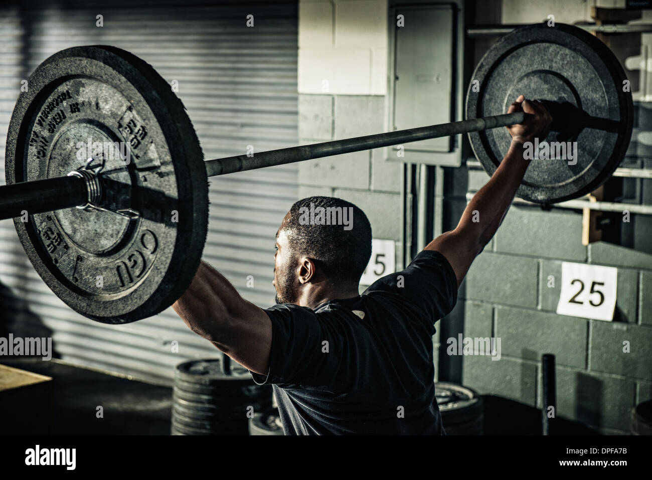 Young man holding up barbell in gymnasium Banque D'Images