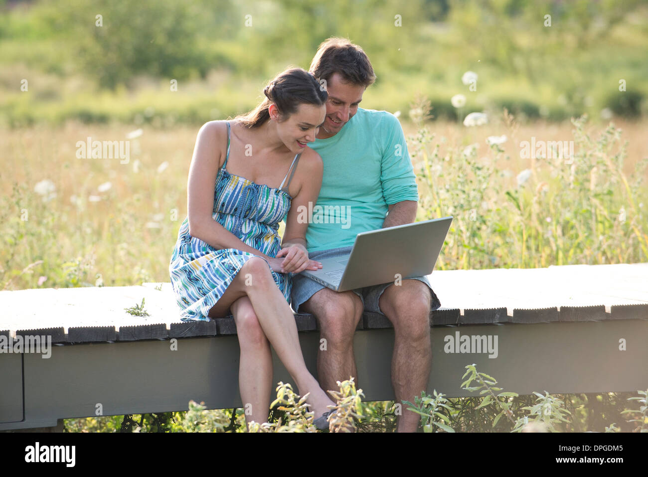 Couple sitting on countryside boardwalk with laptop computer Banque D'Images