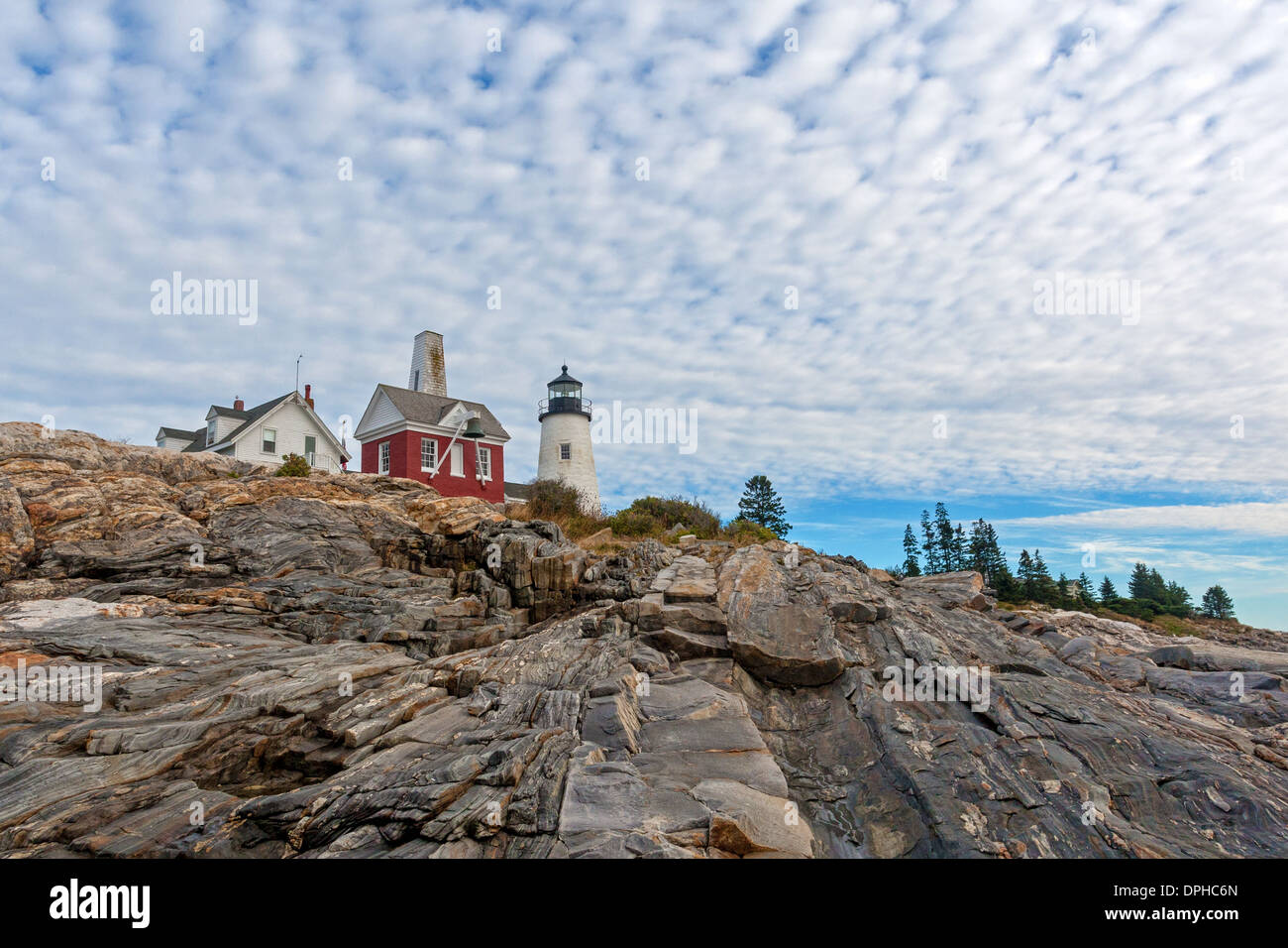 Le phare à Pemaquid Point, Maine avec ciel nuageux au-dessus et les corniches rocheuses massives à l'avant-plan. Banque D'Images