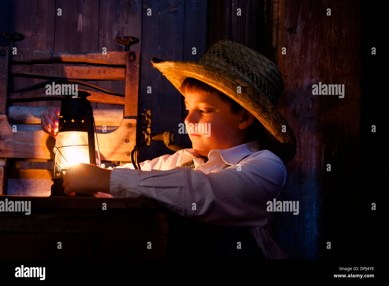 Un petit garçon fermier dans la grange avec une lampe à huile Banque D'Images