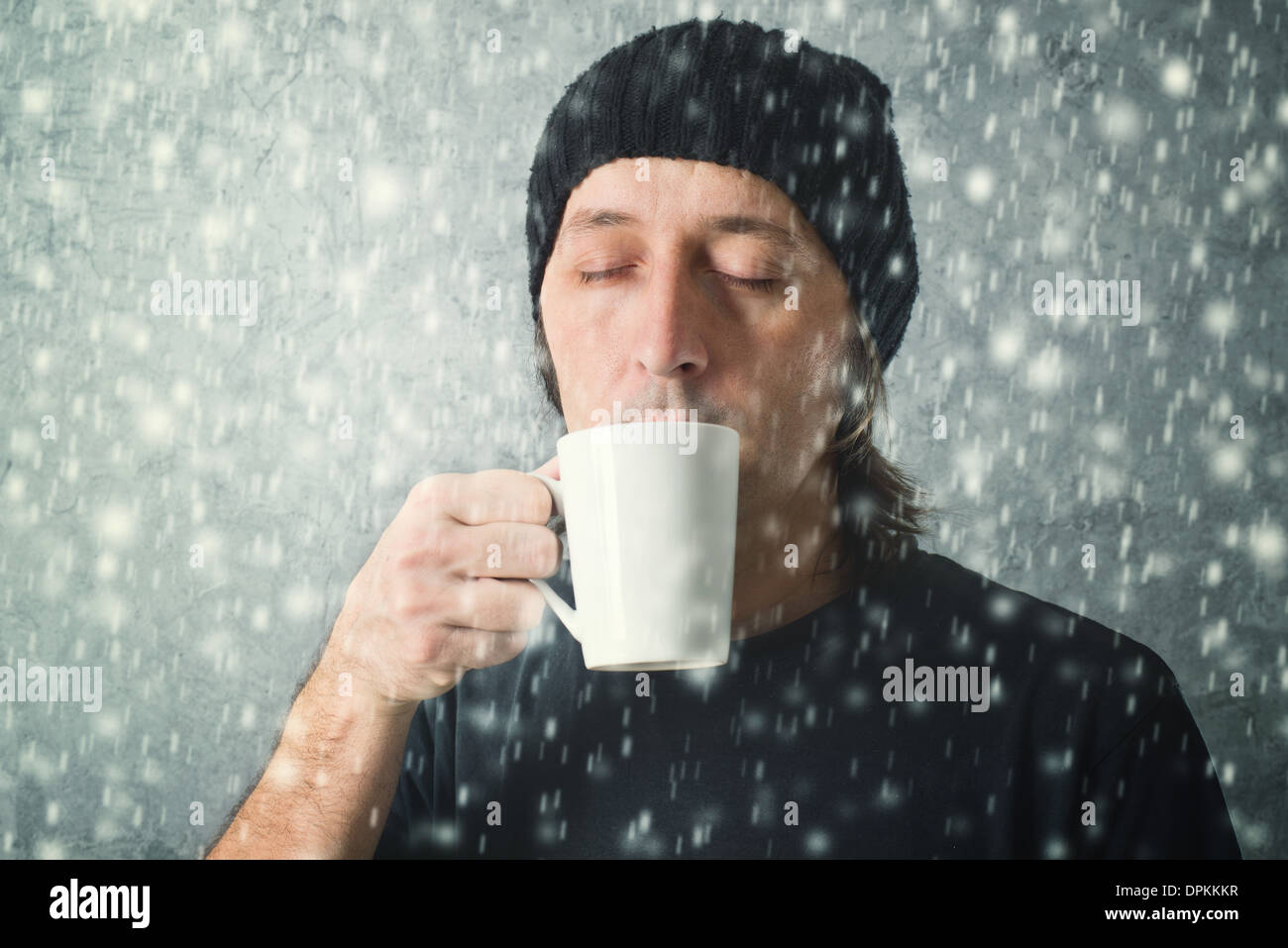 L'homme de boire du thé à partir de la tasse alors que la neige tombe. Banque D'Images