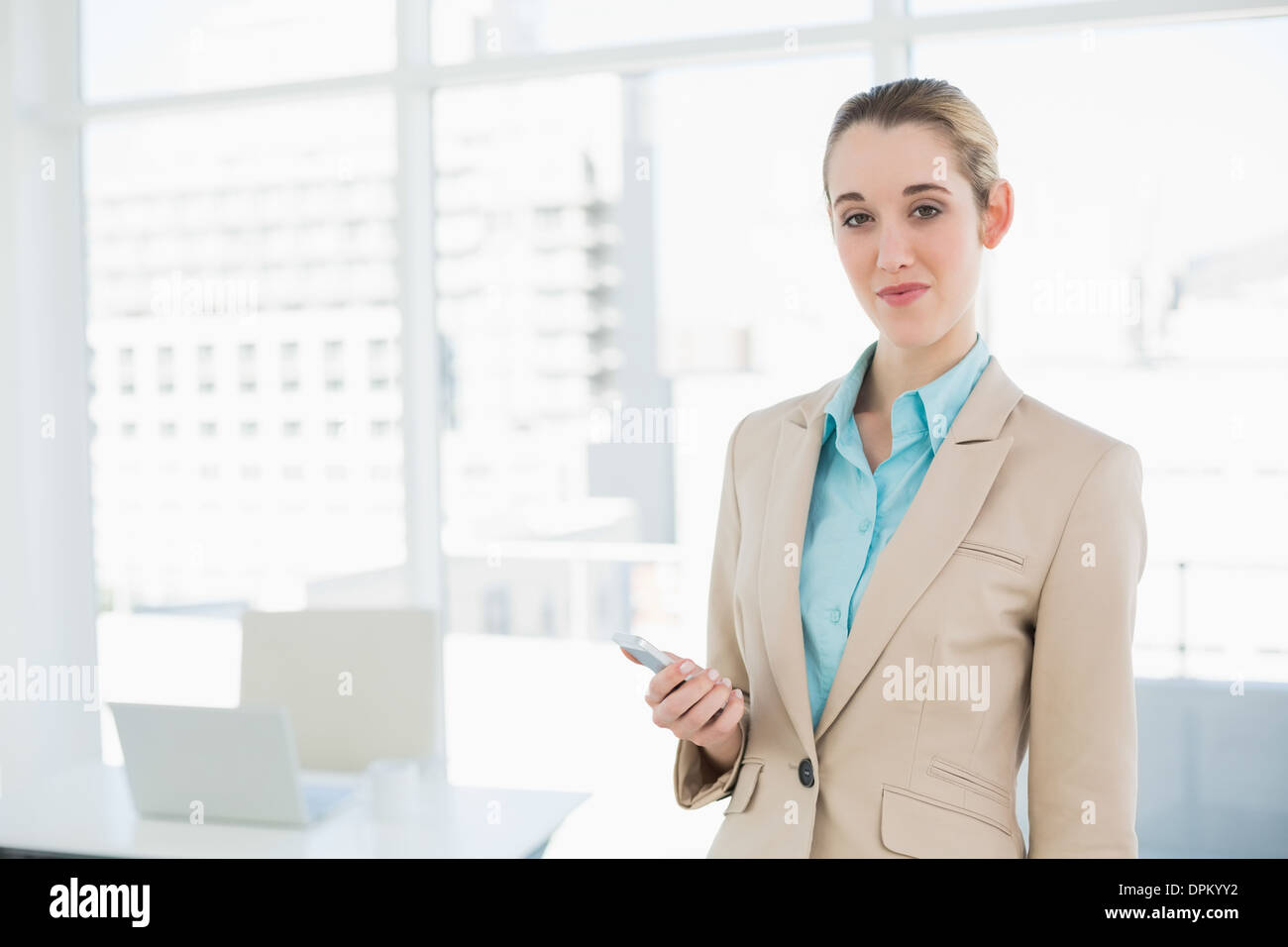 Assez chic businesswoman holding her smartphone smiling at camera Banque D'Images