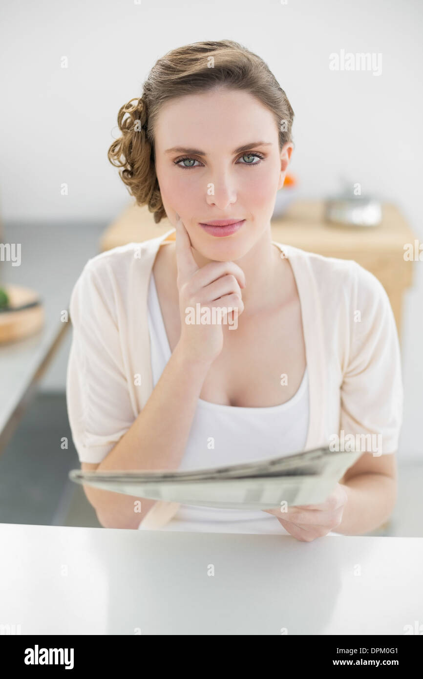 Superbe femme penser assis dans sa cuisine holding newspaper Banque D'Images